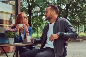 A couple dating drinking coffee, sitting near the coffee shop. Outdoors on a date.